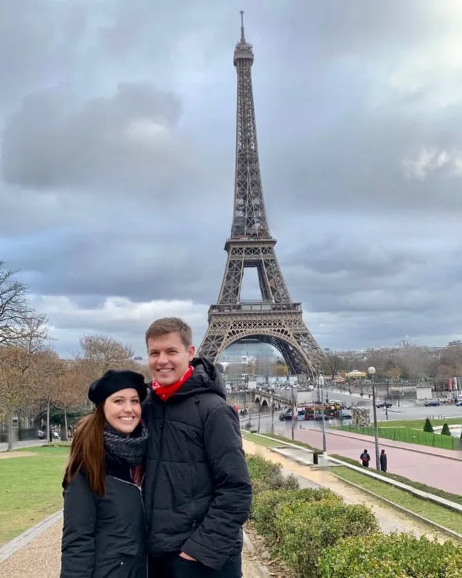 Picture of Amber and spouse wearing jackets in front of the Eiffel Tower