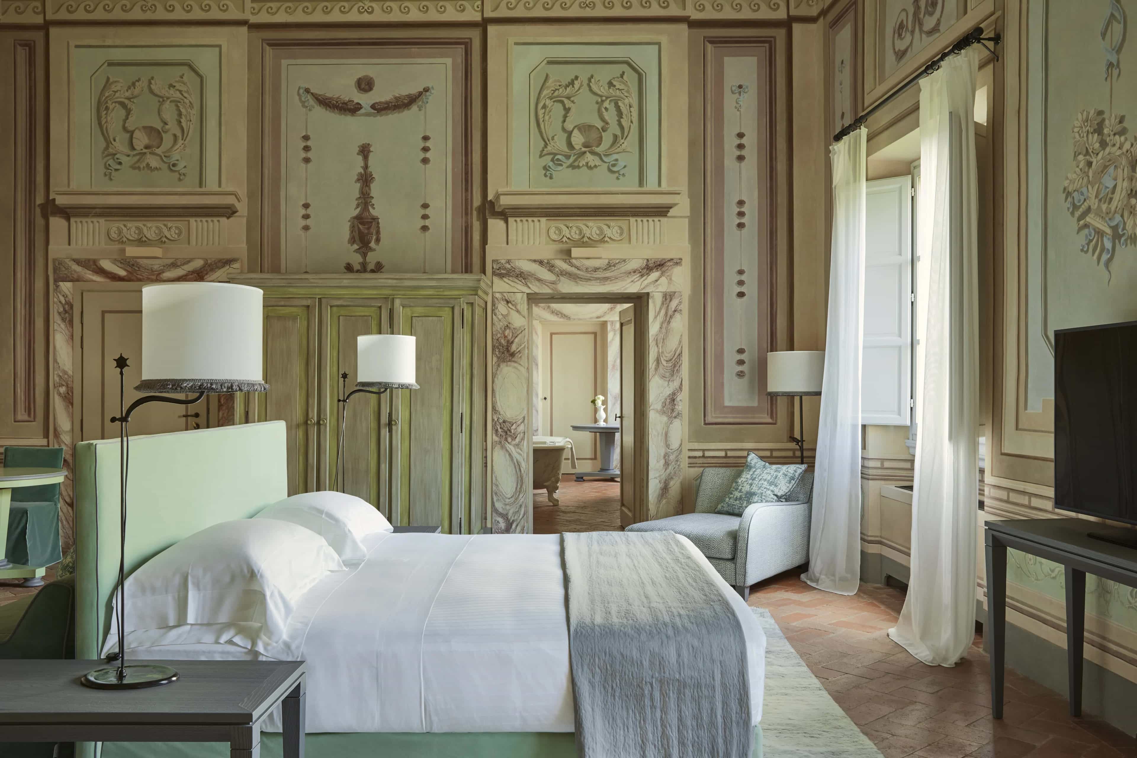 Frescoed walls in muted greens, browns, purples and creams with a bed in the middle of the room
