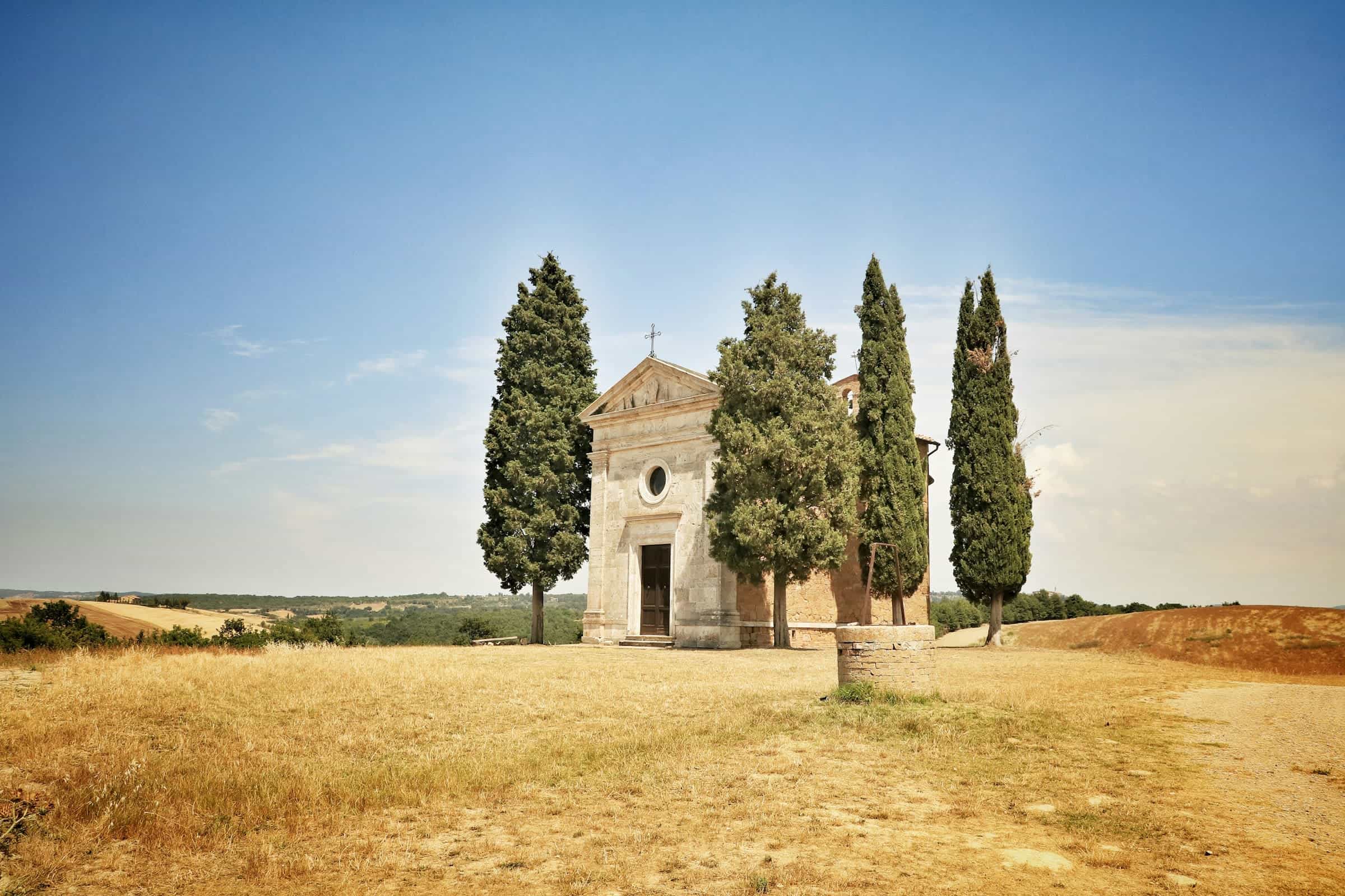 Small white stone church surrounded by green trees during day on a hilltop