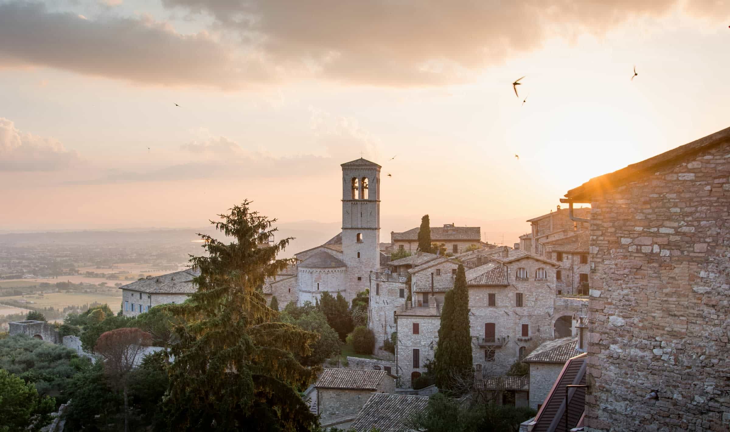 Sun peaking above the rooftops with a view of a hillside town of white buildings