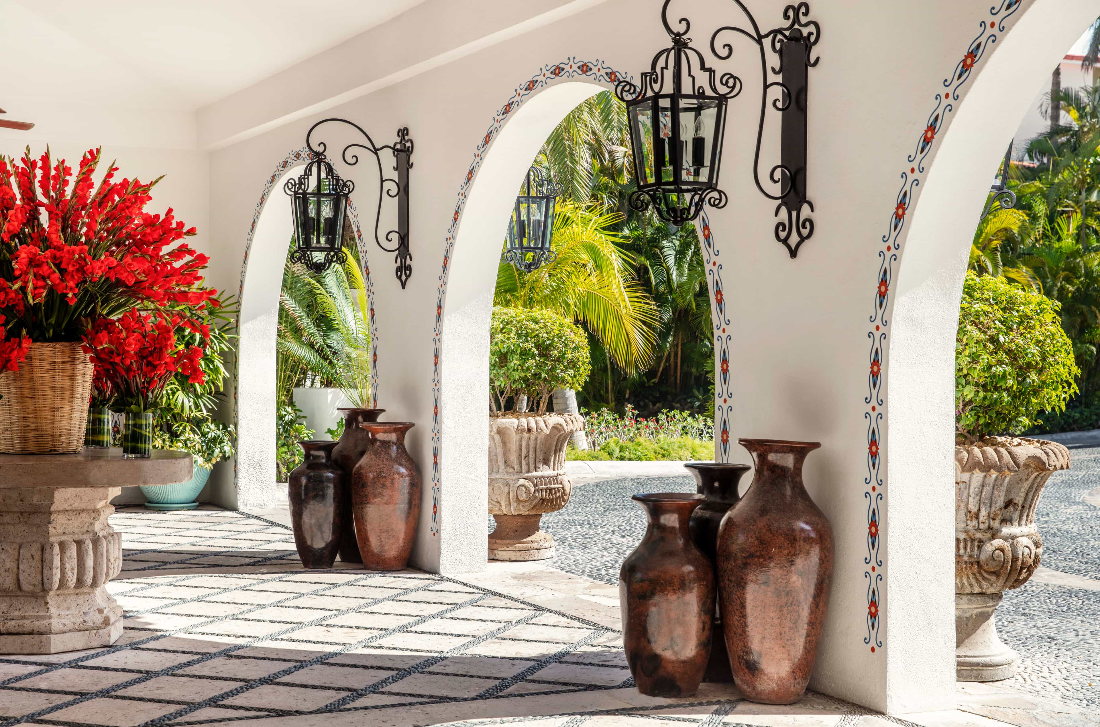 A hotel lobby area with white archways, bright flowers, and antique standing vases