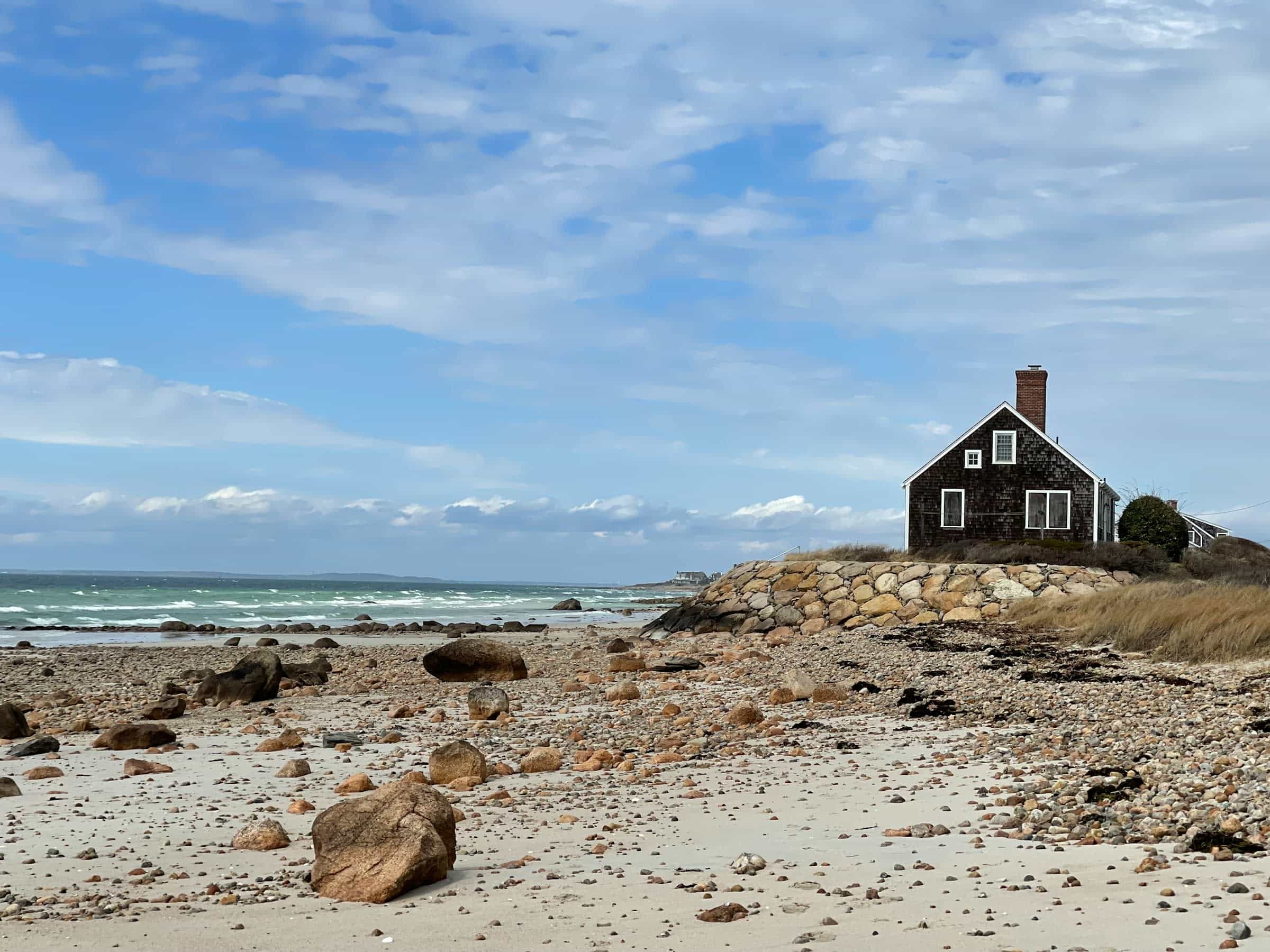 a dark brown wood house sitting on top of a sandy beach next to the ocean at daytime