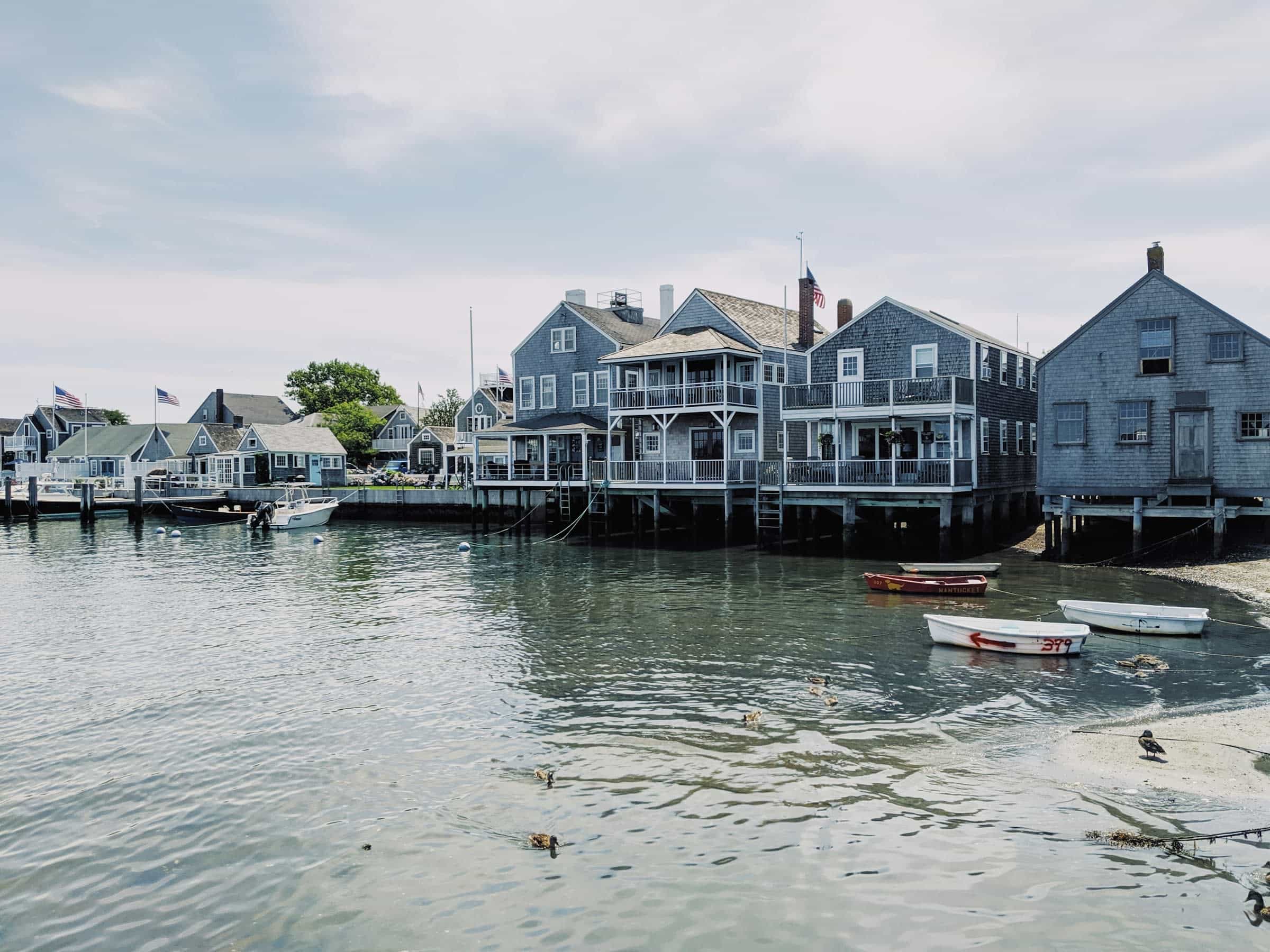 white and grey wood buildings lining a small harbor with a few white row boats