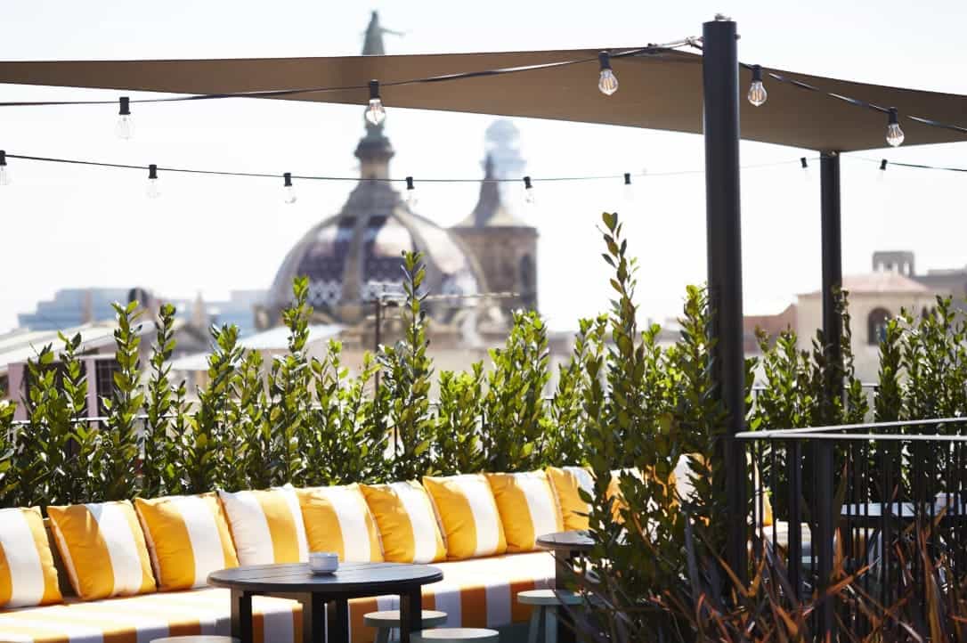 A rooftop terrace with yellow-and-white-striped cushions, string lights and a dome-shaped building in the background.