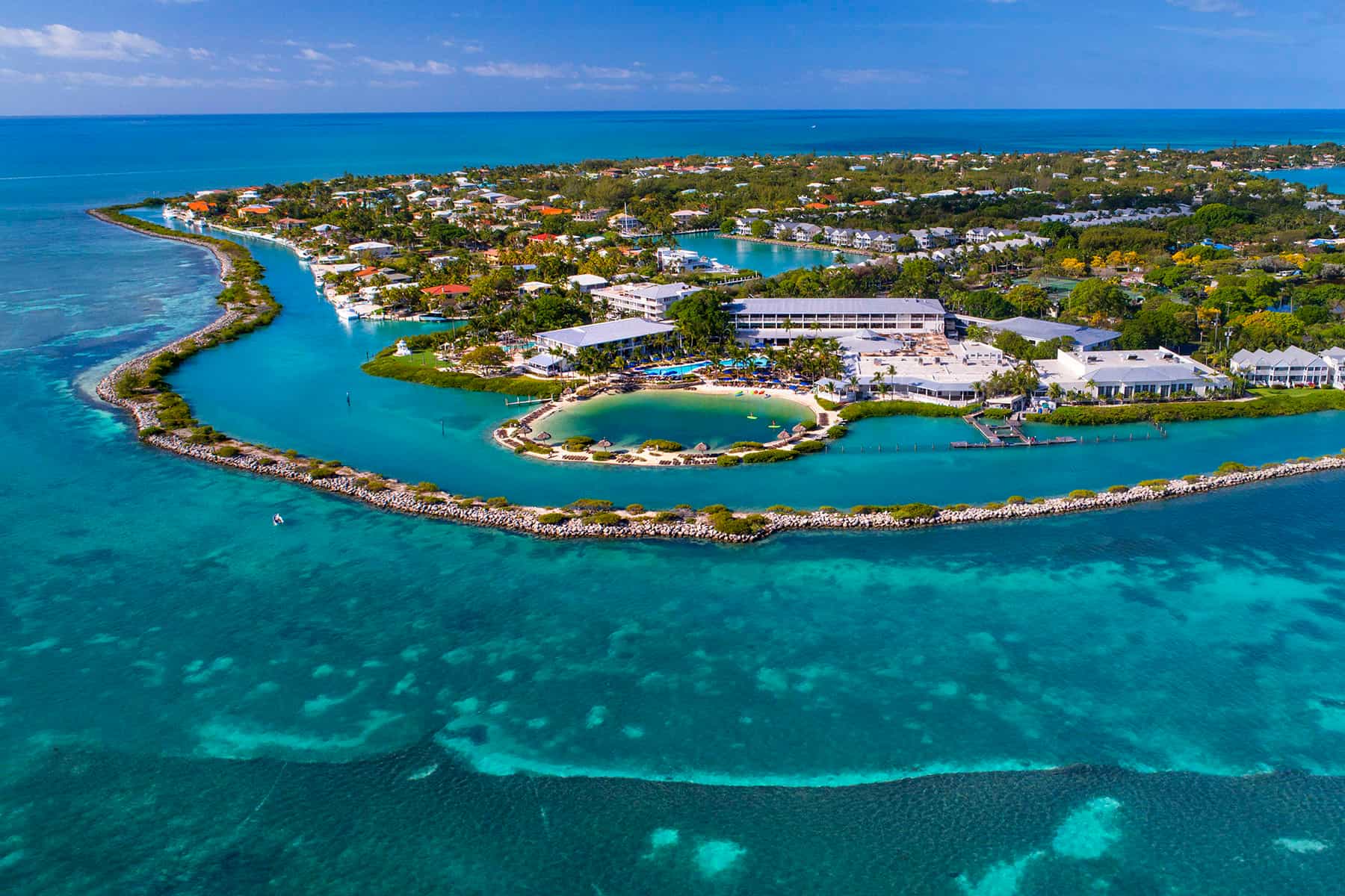 Aerial view of Hawks Cay resort island surrounded by turquoise ocean waters, featuring sandy beaches, pools, resort buildings, and lush greenery.