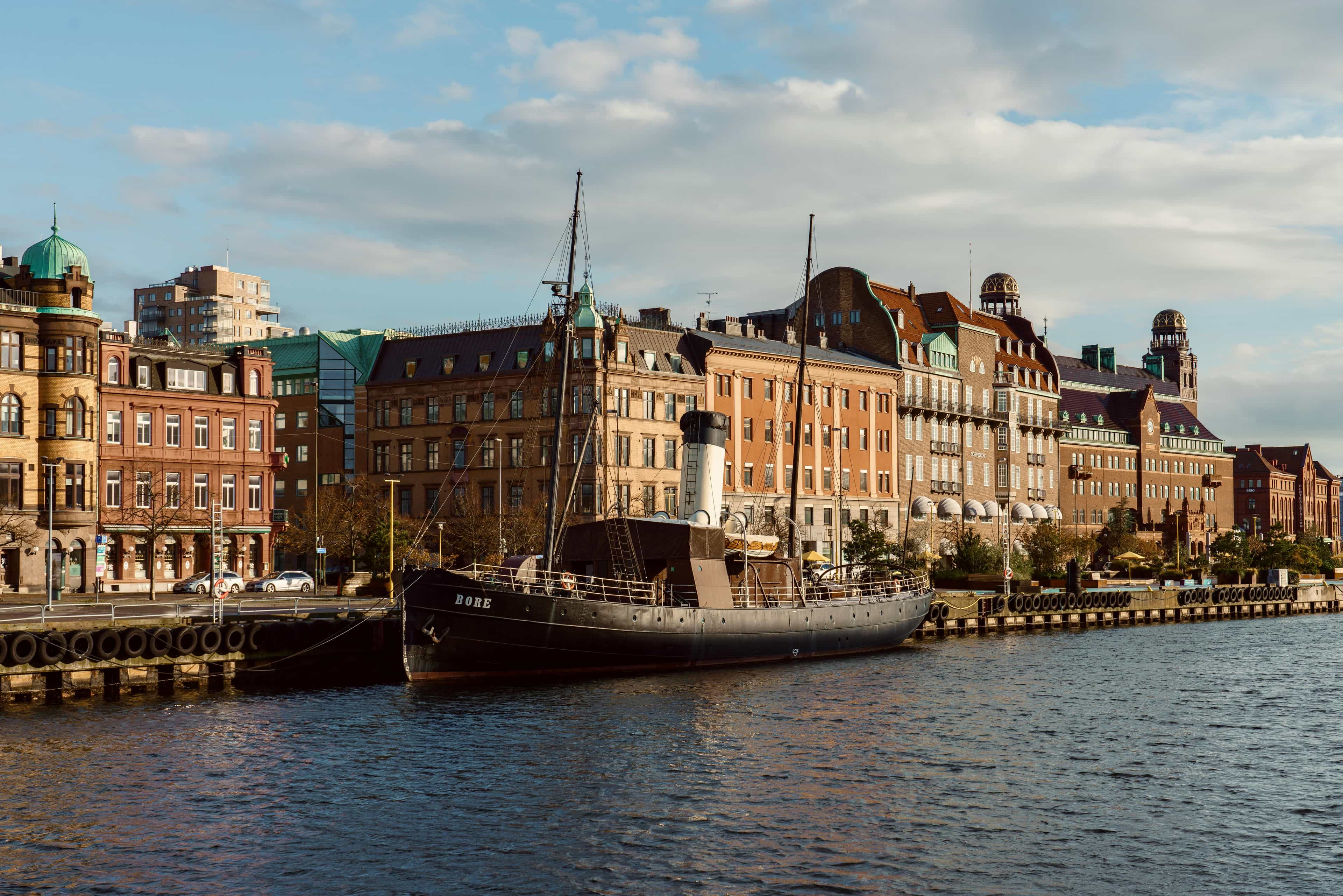 a 19th century icebreaker ship docked on a harborside in the city with brick buildings behind during day