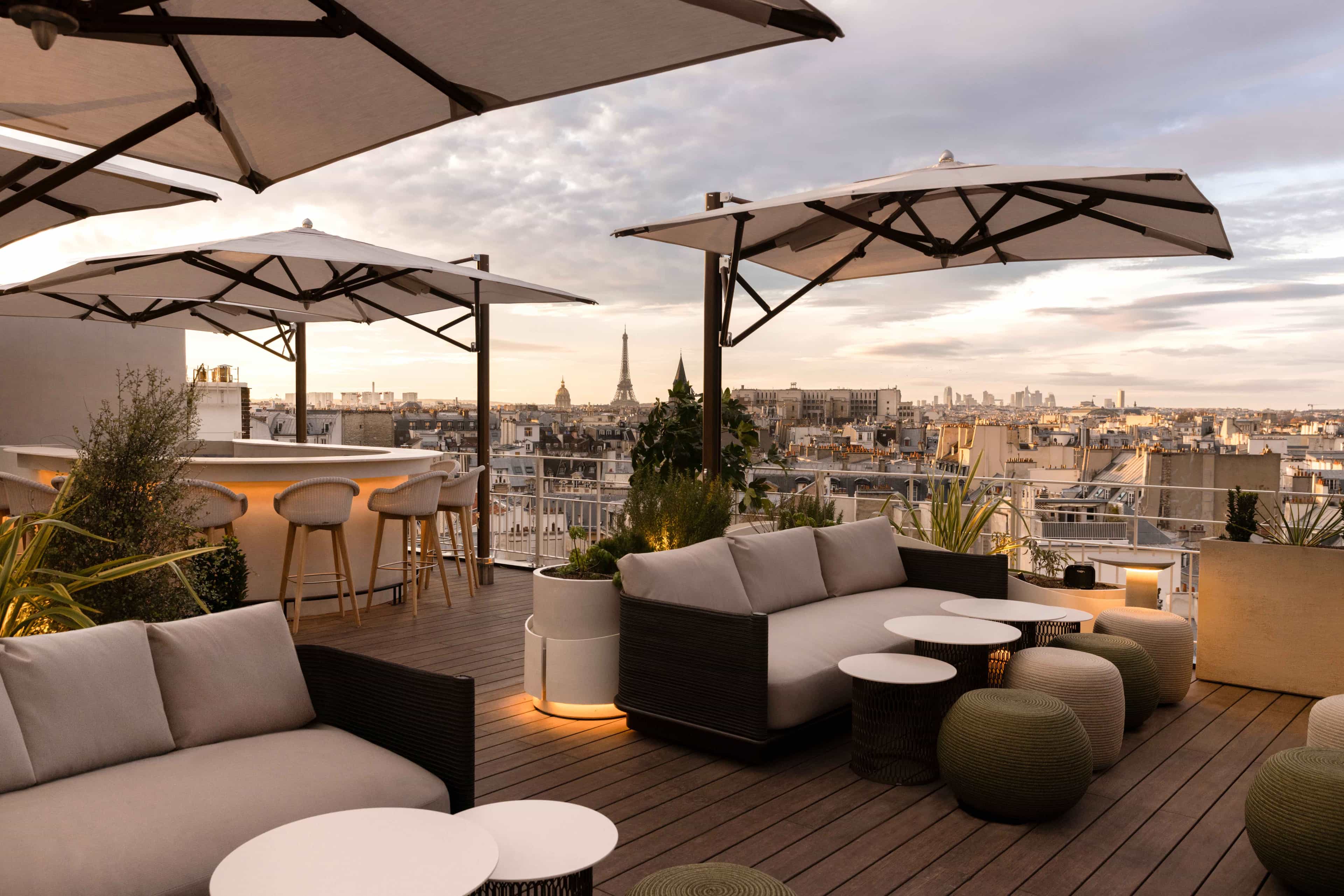 An elegant rooftop terrace with lounge seating and white umbrellas with city views against soft, evening light