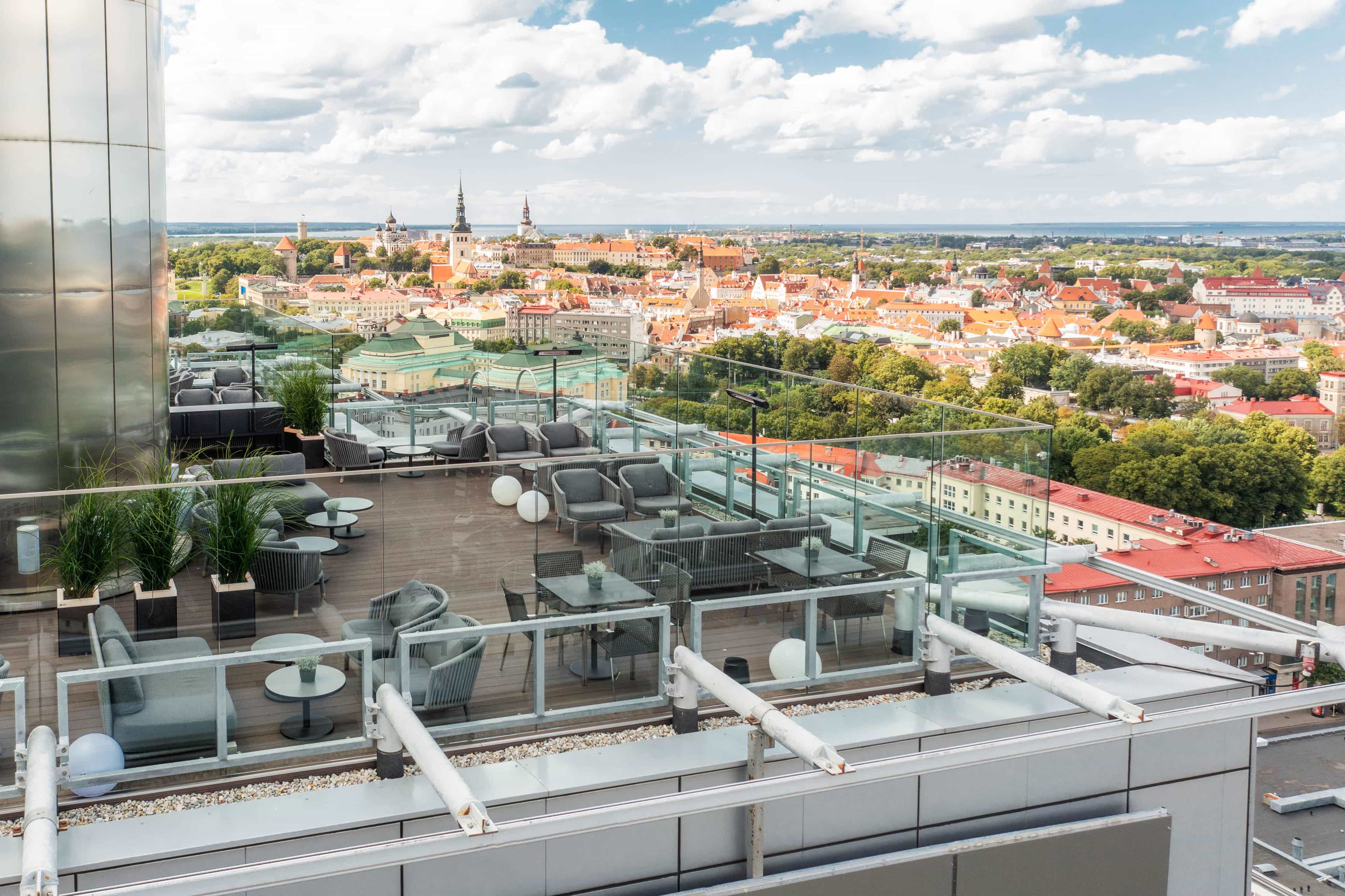 An aerial view of a rooftop bar with grey lounge seating and wooden flooring overlooking Tallinn, Estonia