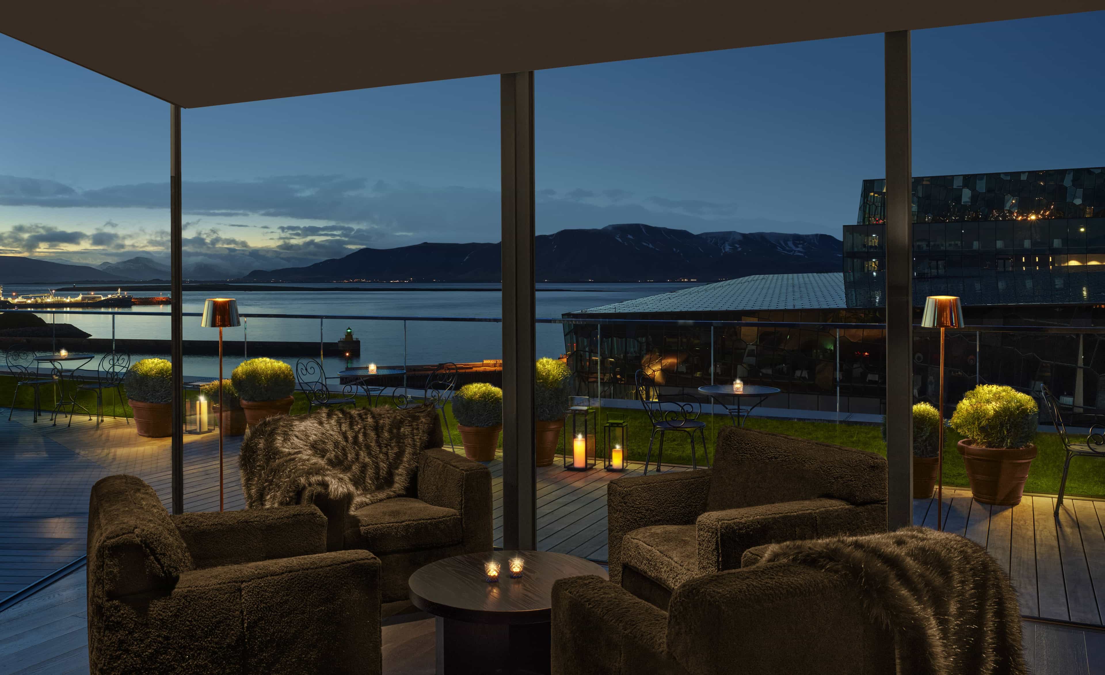 A rooftop at night with warm candle lighting and ocean and mountain views