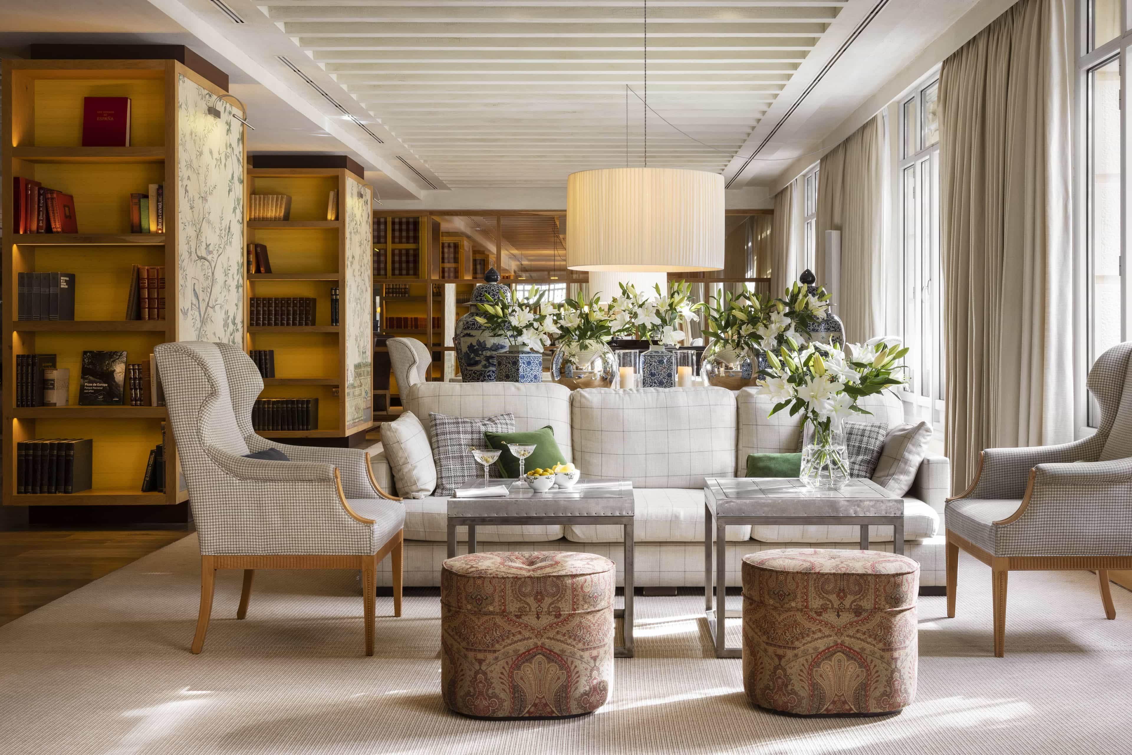 Elegant hotel lounge with patterned armchairs, plush sofa, fresh flowers, and bookshelves creating a cozy, refined atmosphere.