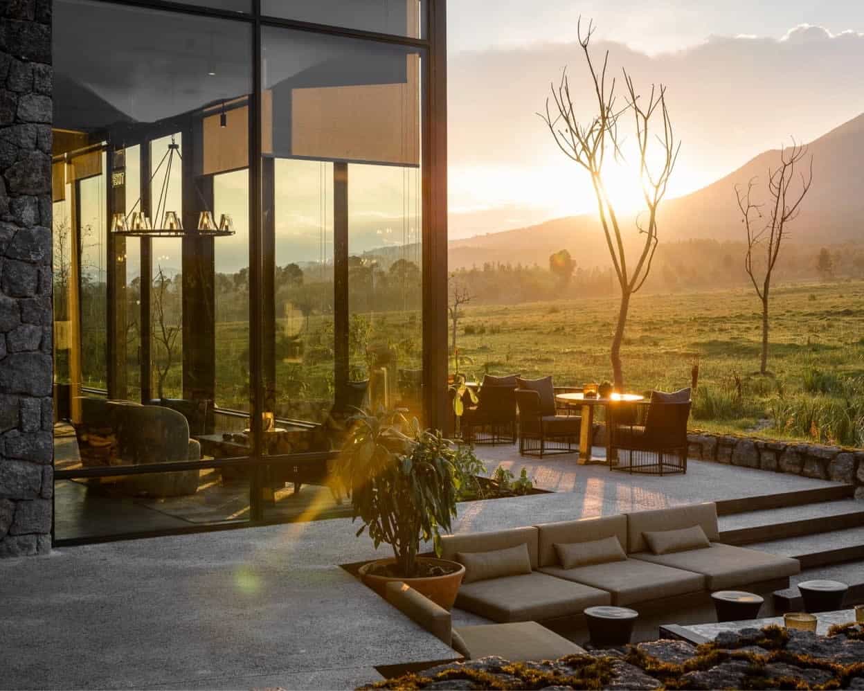 patio with chairs and seating modern outside of a lodge with stone, glass and metal as the sun sets over the mountains in the distance