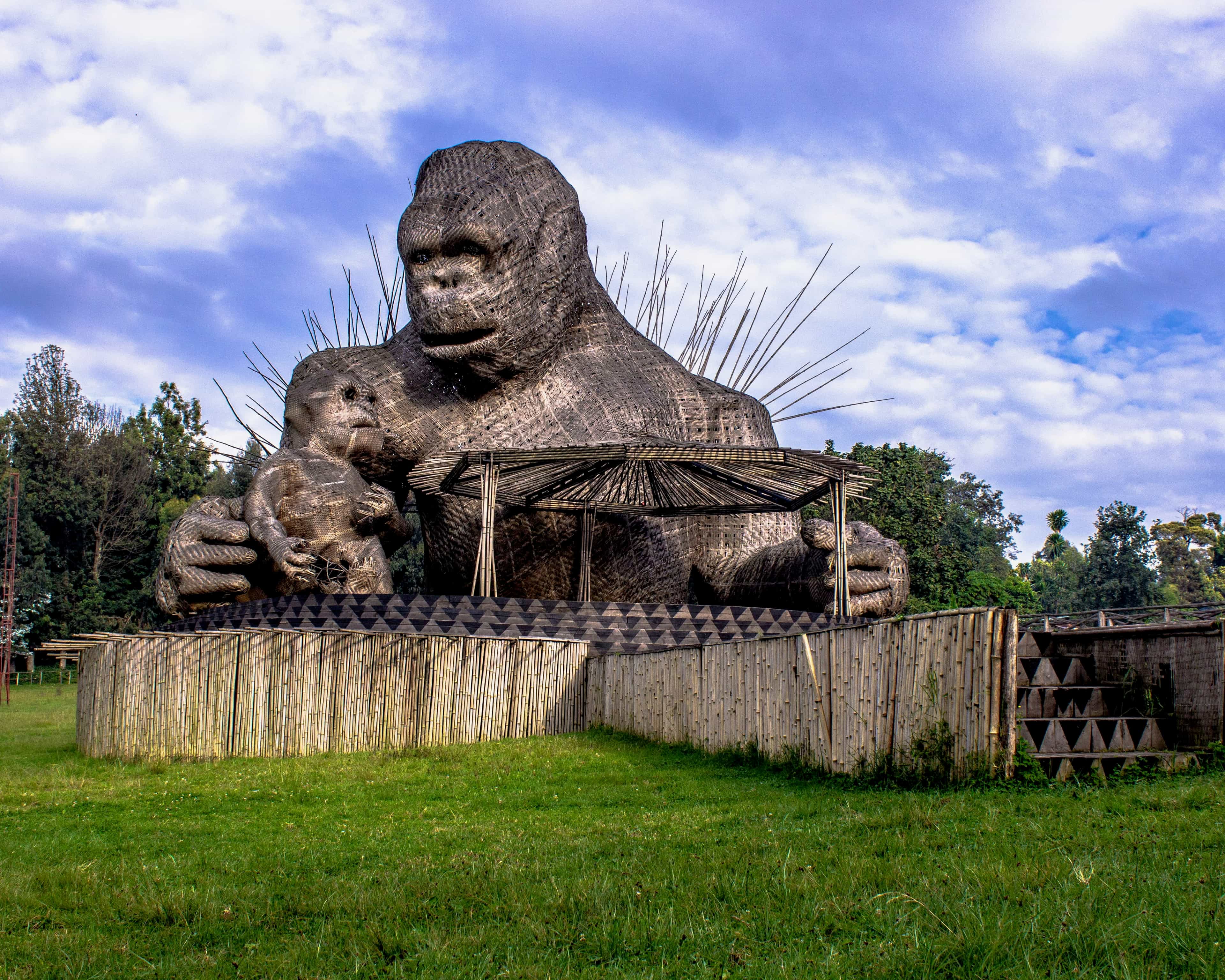 a wooden gorilla and baby gorilla monument with green grass and blue sky