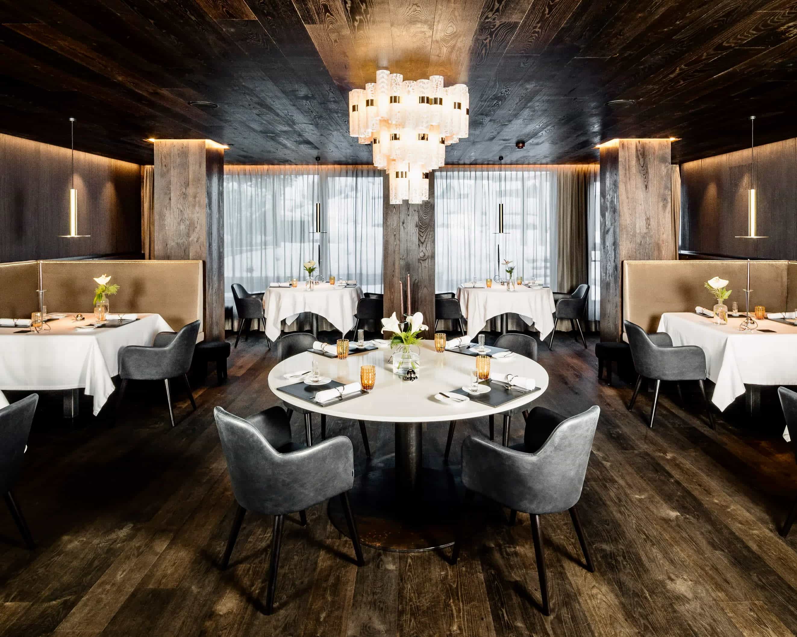 restaurant with white tables, grey chairs, black wood floor and ceiling, and modern chandelier