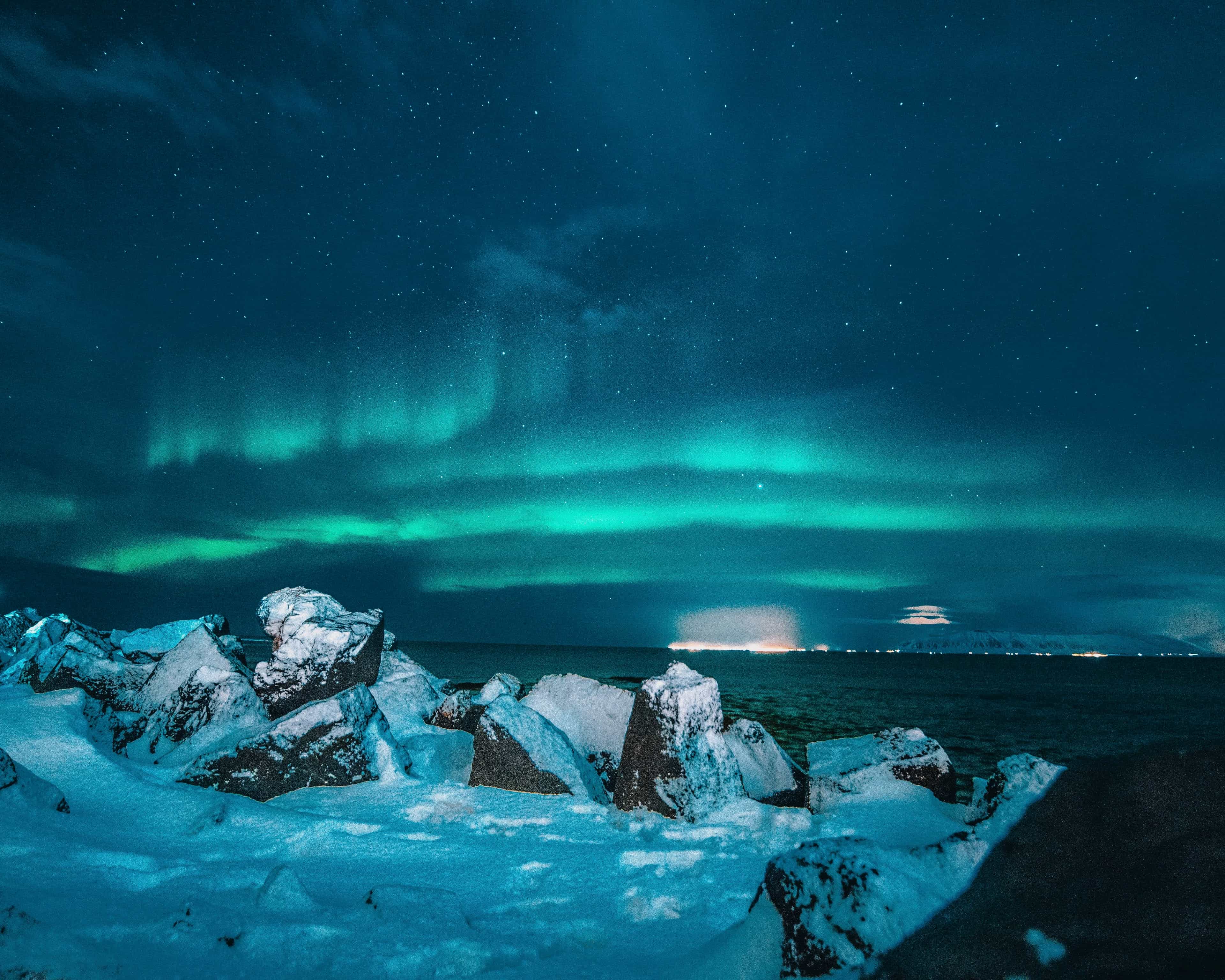 green aurora in a dark blue sky with snow covered ground in the foreground