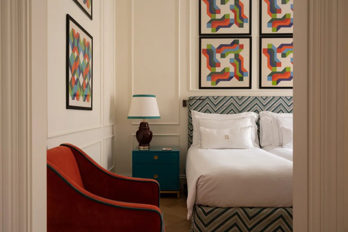 A room at the Palazzo Ripetta, with geometric artwork on the walls, a blue headboard and a red chair.