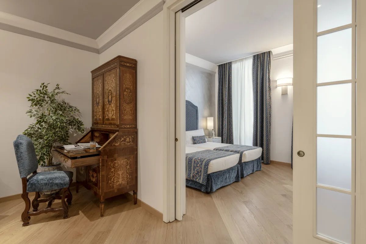 A suite at the Rivoli Boutique Hotel, with a living room with wooden desk and a blue-accented bedroom.