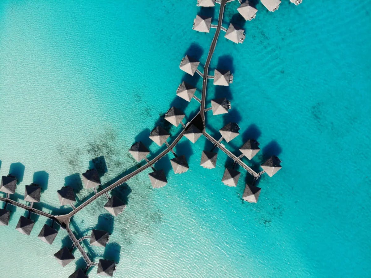 A drone view of a cluster of overwater bungalows in the crystal, clear sea.