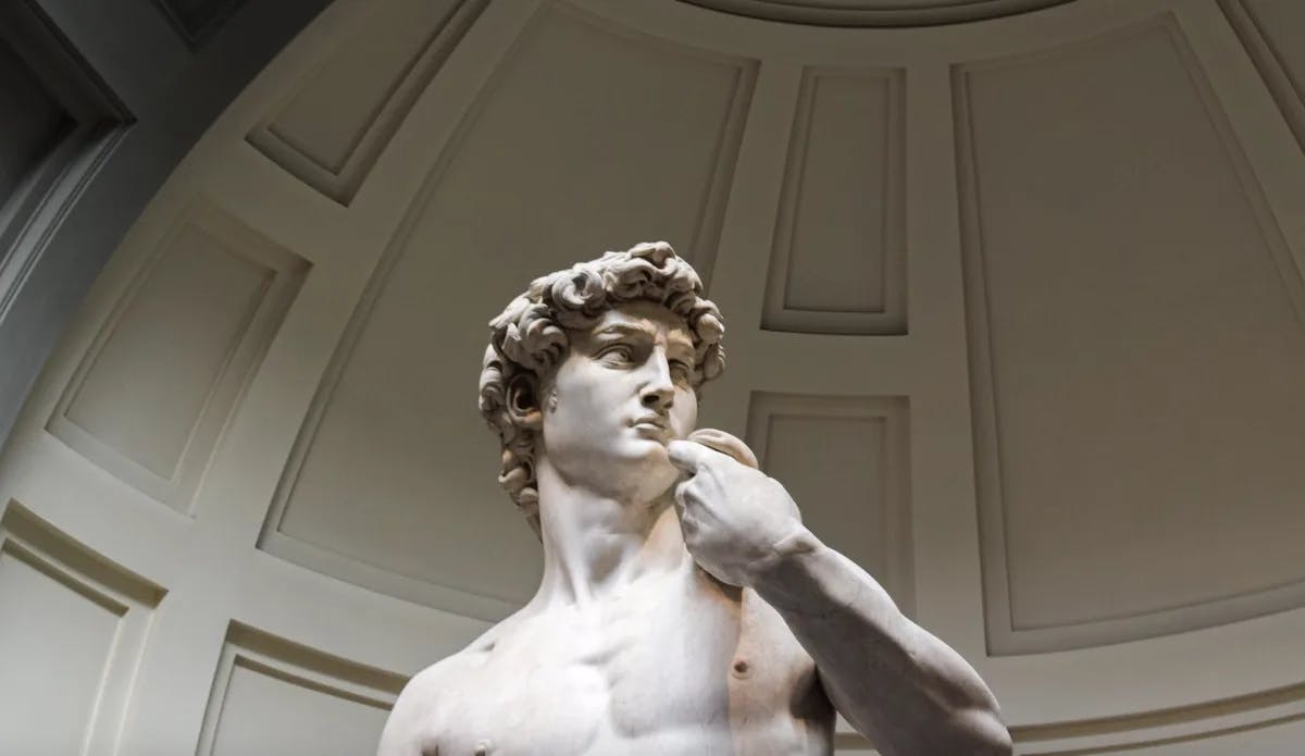 A view of the Statue of David lit up inside of a museum gallery.