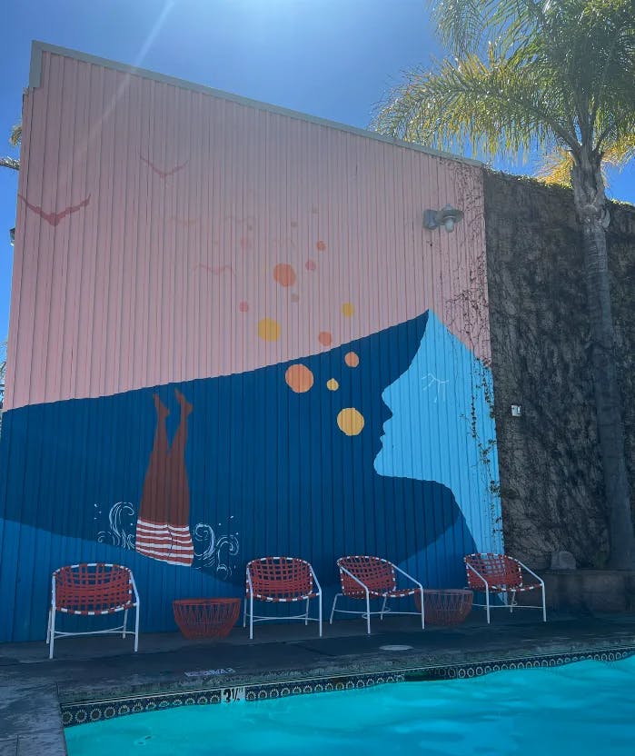 A mural of a person diving into a pool next to a swimming pool with red chairs lined up next to it.