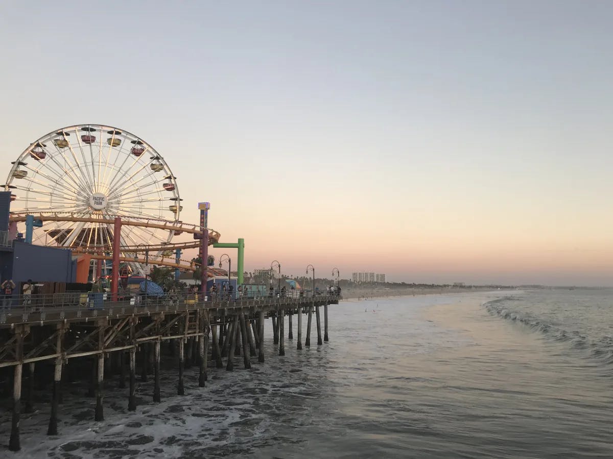 A view of the Santa Monica Pier next to the sea with a pink sunset in the background. 