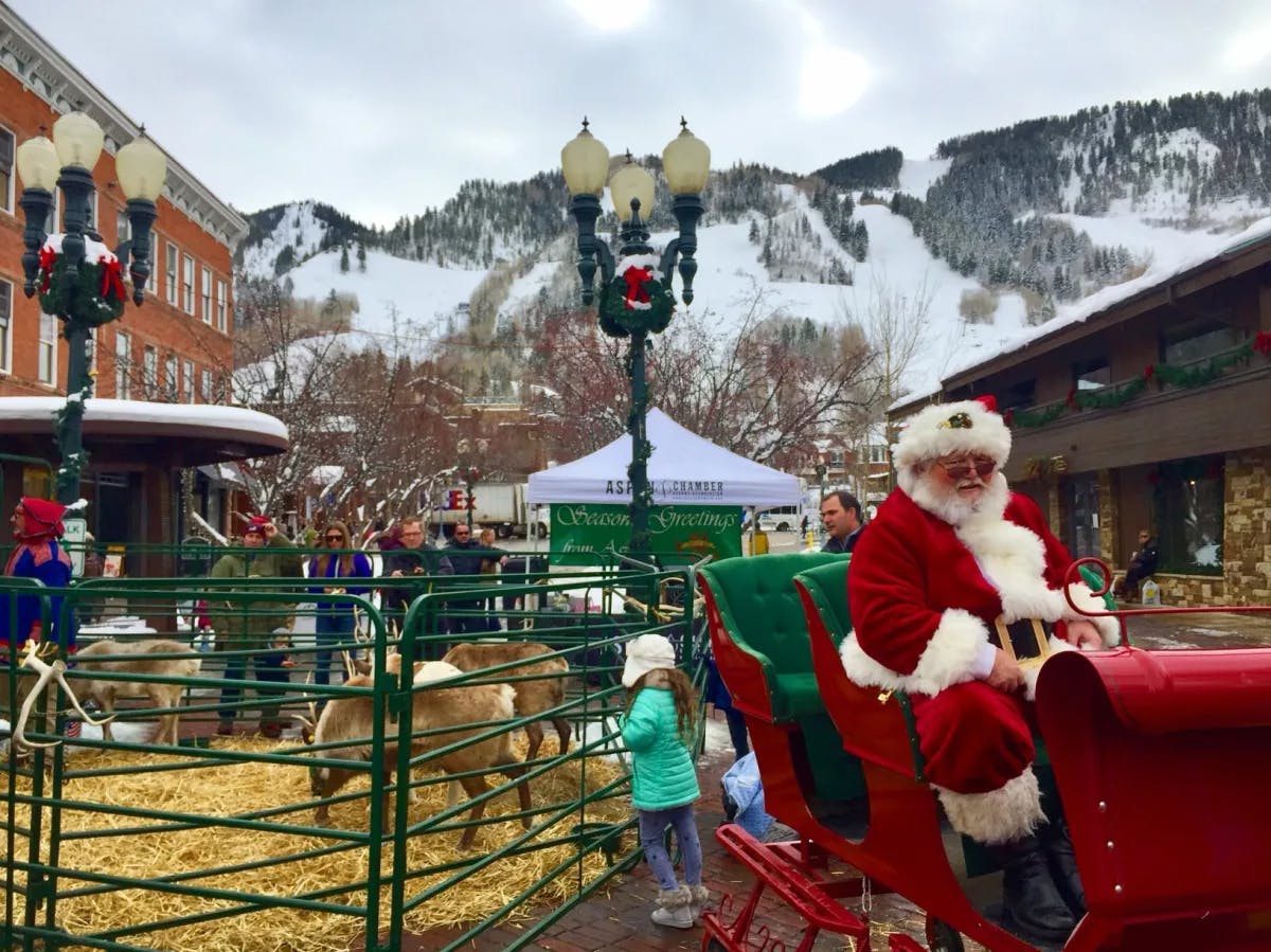 Santa Claus in its red trolley ride with reindeers at the back amidst snow covered mountains.
