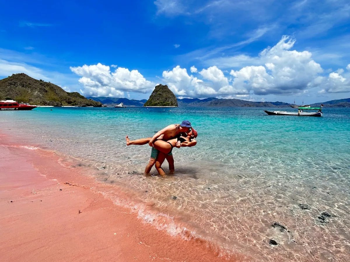 A couple kissing at a beach with pink sand. 