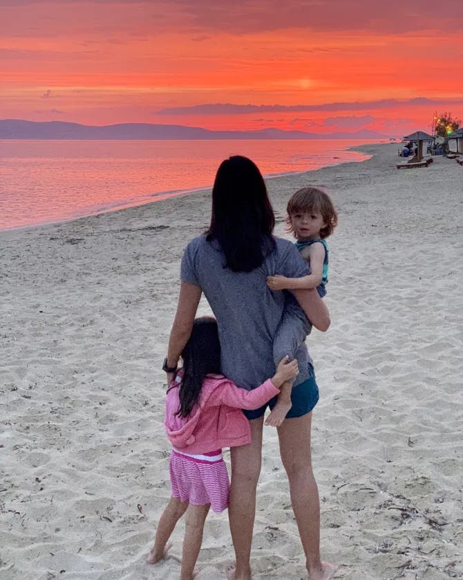 Nadiah on the beach with her children and an orange sunset in the distance. 