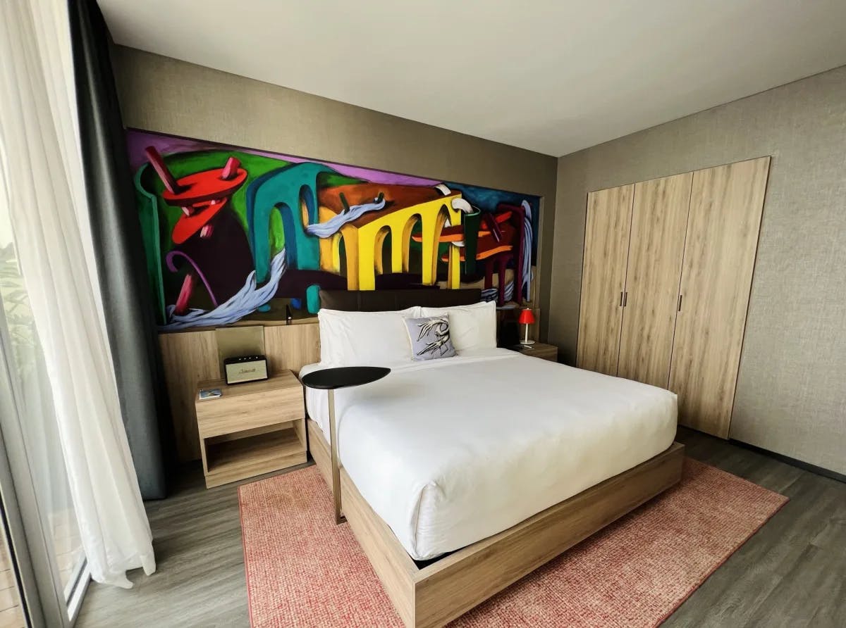 A room with bed and a colorful painting on the wall. 