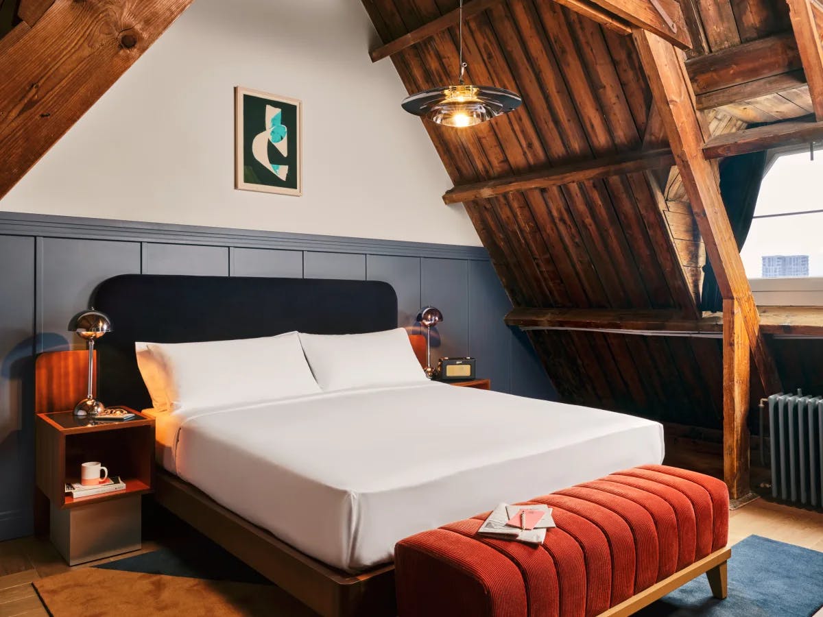 A bedroom at the Hoxton Lloyd Amsterdam with timber ceilings, a blue headboard and an orange bench.
