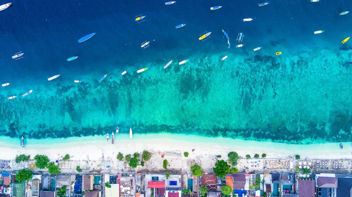 Aerial picture of a a beach with boats on its clear water. 