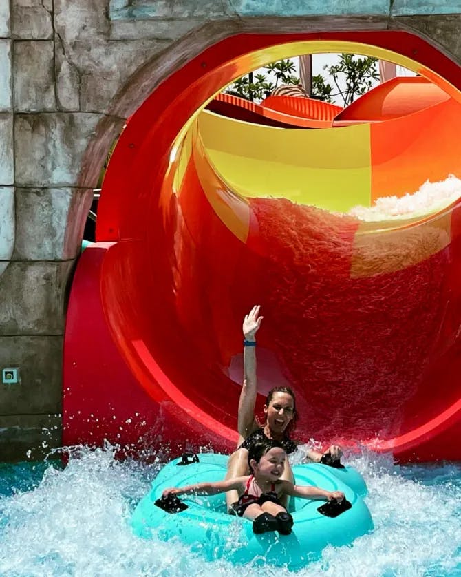 Jennifer and a child going down a red water slide.