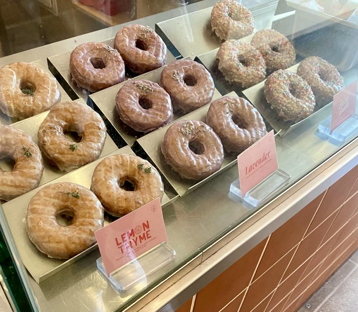 A glass case full of donuts with pink notecards with flavor labels in front of them. 