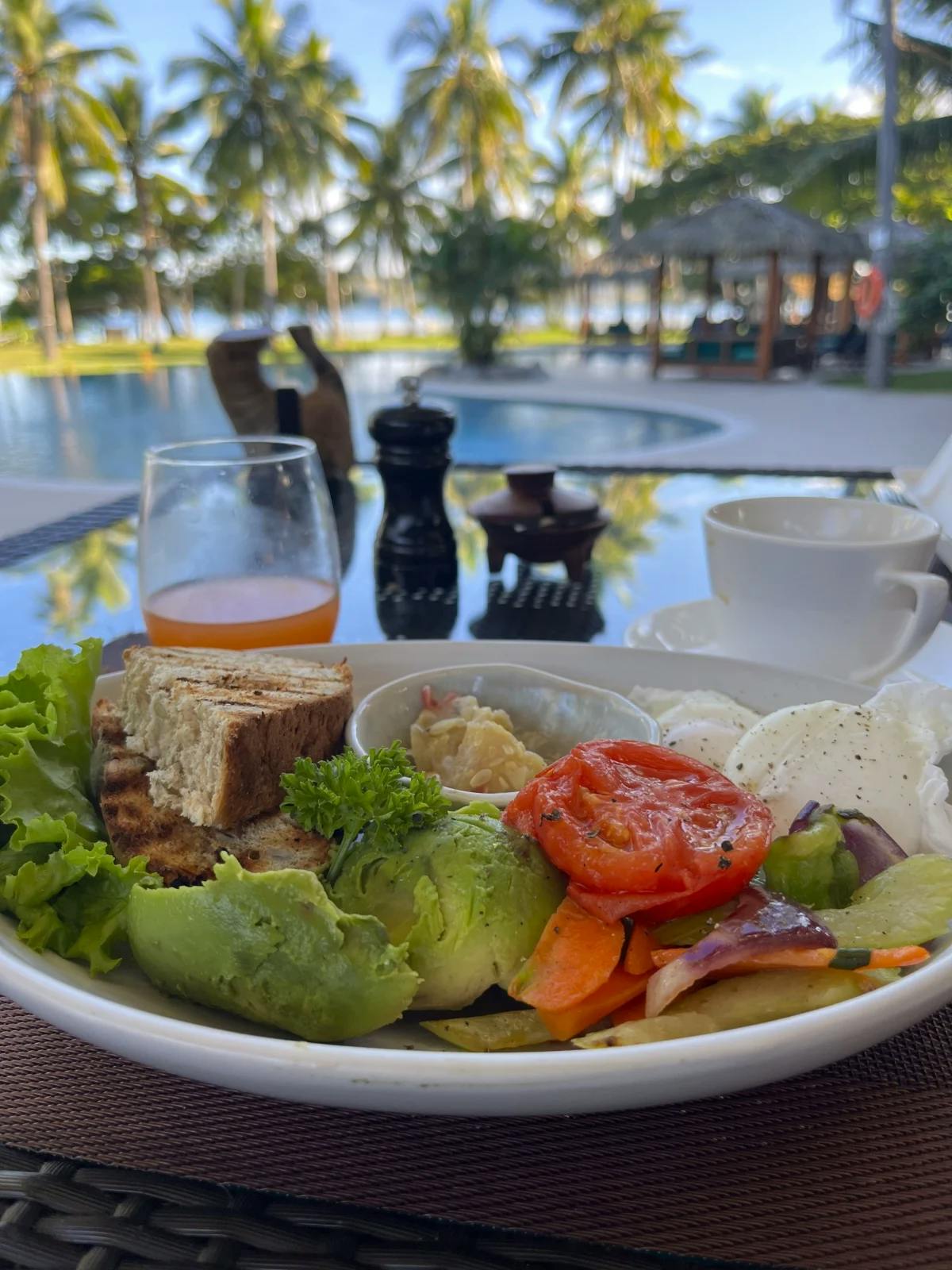 A plate of vegetables on a table overlooking the pool with palm trees in the background