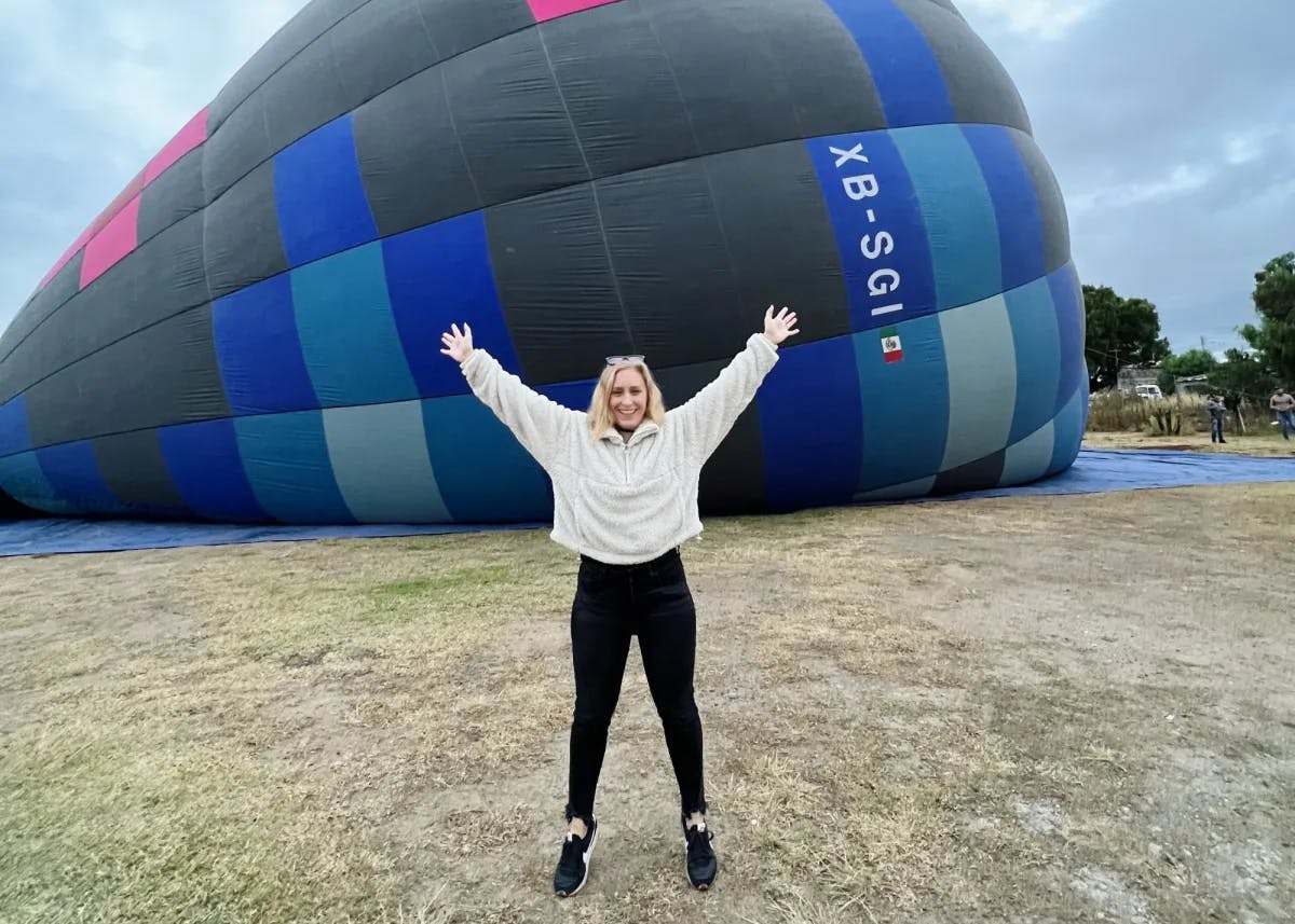 A woman posing with arms up in front of a hot air balloon. 
