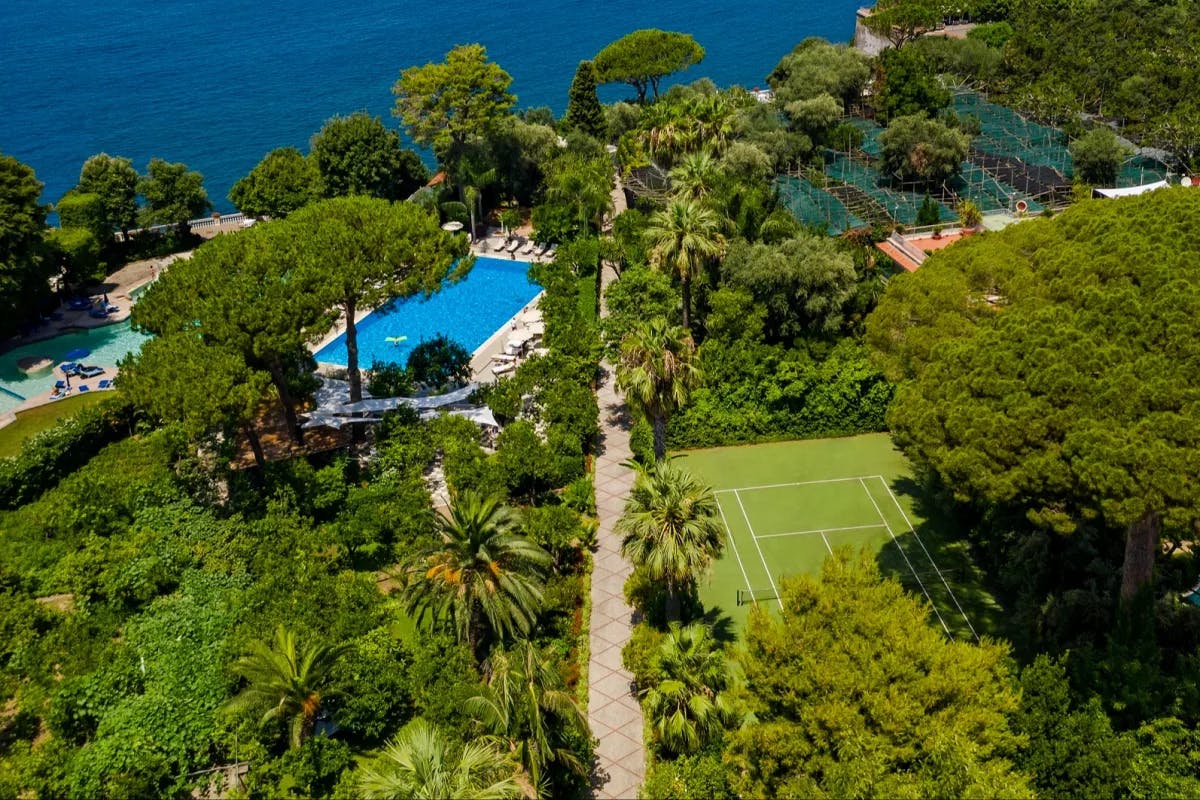 aerial view of a pool and a tennis court amid lush seaside gardens