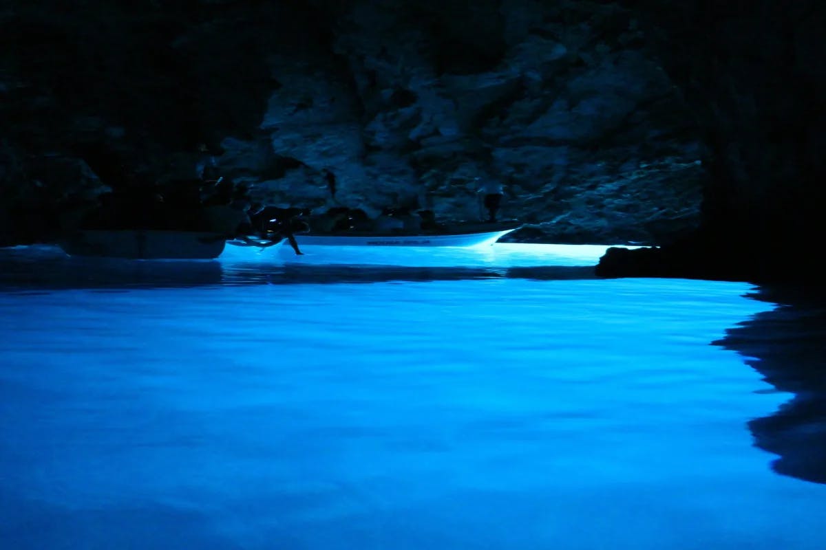 A boat in the blue-colored water inside a cave at nighttime.