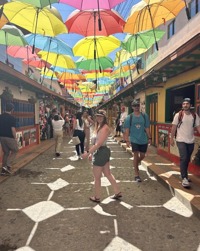 Travel advisor Samantha standing in the street in green shorts and white top with colorful umbrellas hanging above