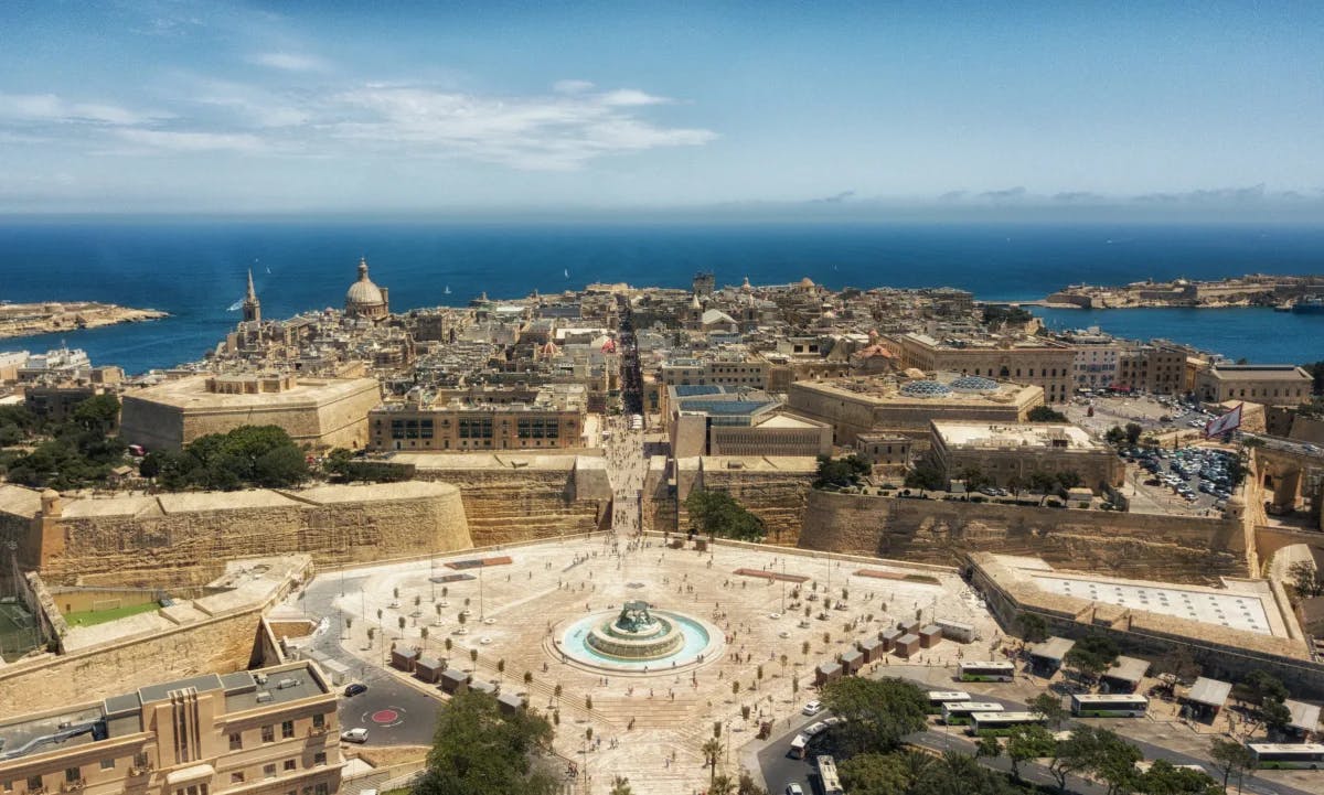 An image of a city overview with a gorgeous city center, light stone work, various buildings and structures as well as the blue sea in the distance. 