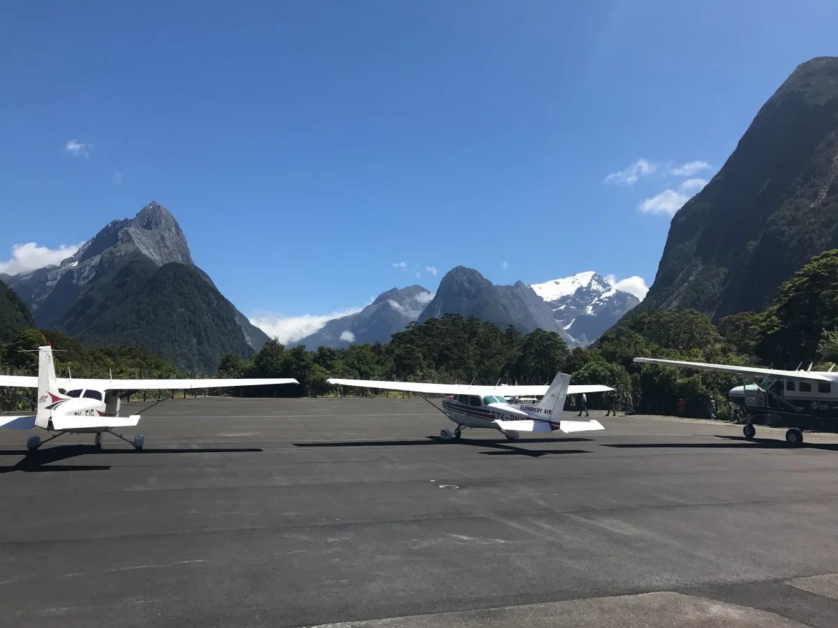 A picture of three white airplanes parked on a runway near snow-capped mountains during daytime.