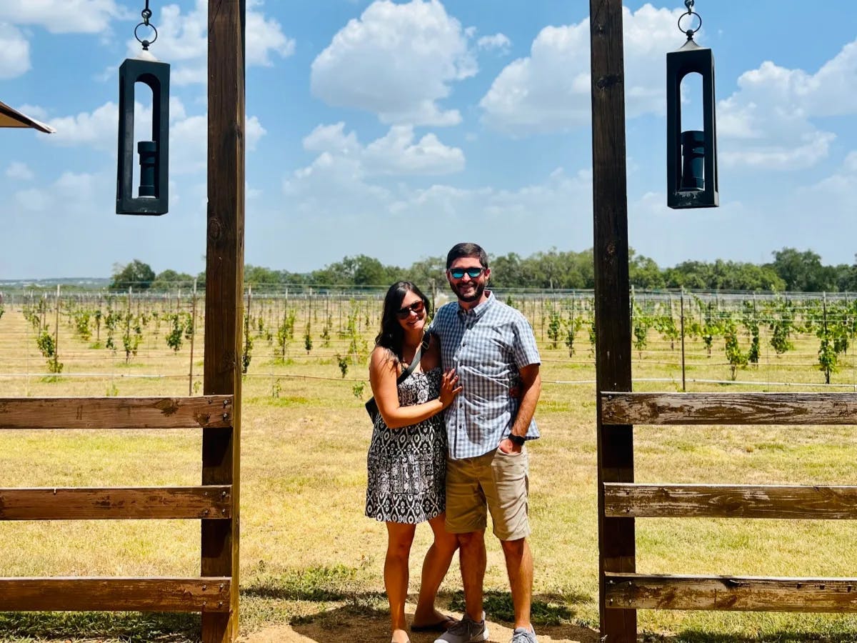 A man and woman standing in front of a vineyard.