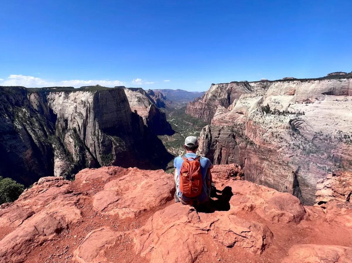 A man with brown backpack sitting on top of mountain.