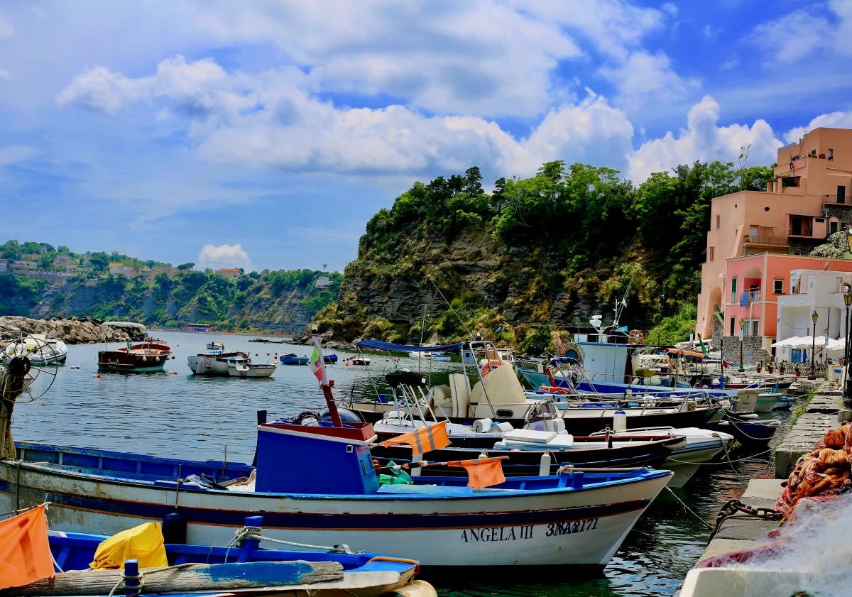The marina of Procida with small blue and white boats docked and picturesque buildings