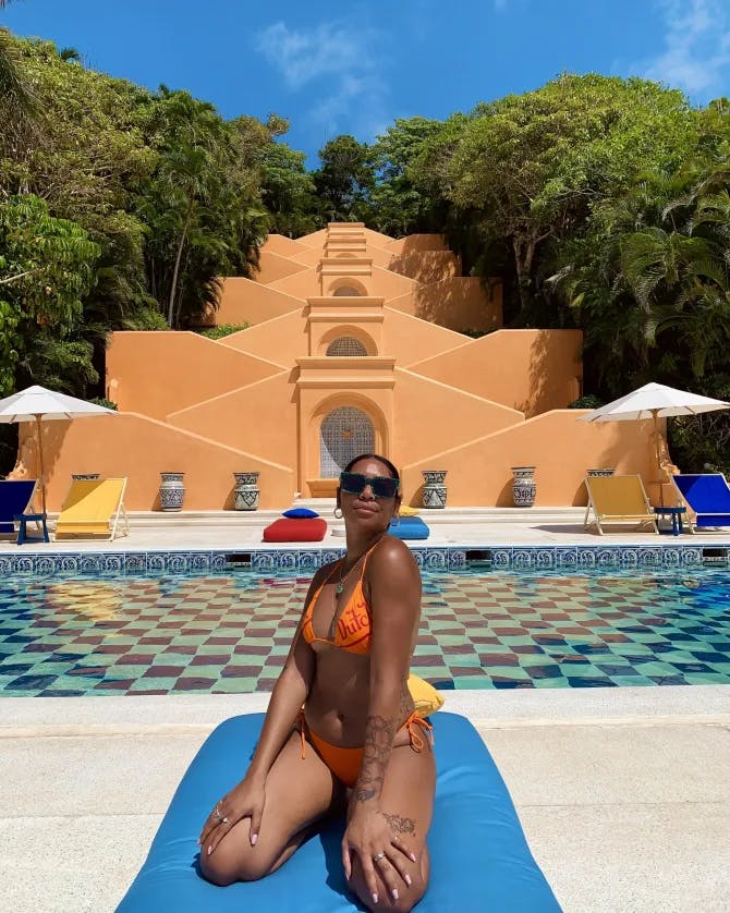 Travel advisor sits on a blue towel in a orange bikini at a hotel pool