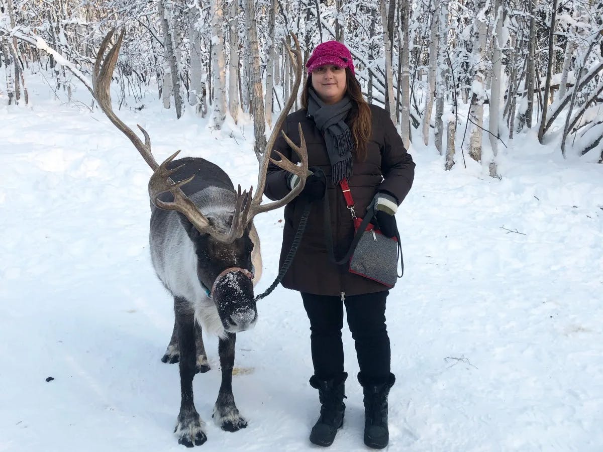Fora Advisor Jonna Robertson in a black snow suit and pink hat standing next to a reindeer