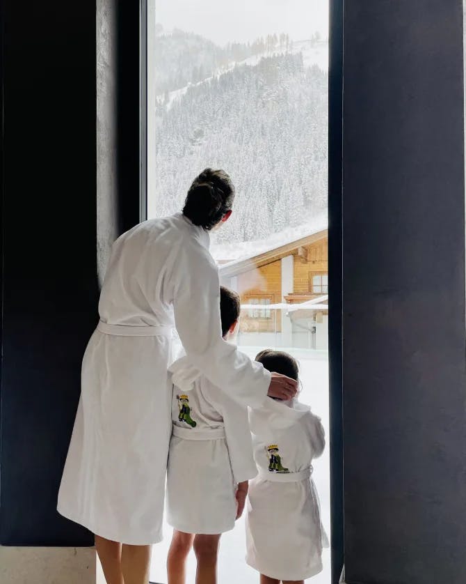 A photo of Jennifer and her two children looking out of a tall window and wearing white robes. 