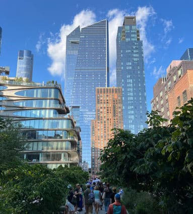 Low-angled shot of old and new buildings in New York with people walking on a walkway in between