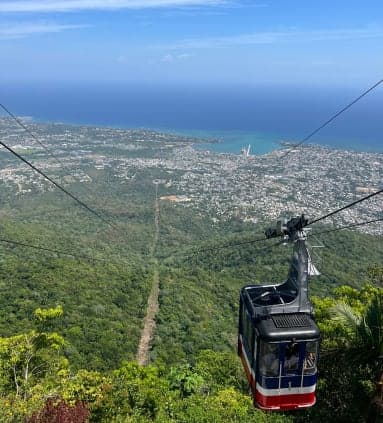 An aerial view of a cable car moving down a hill towards a city with the ocean in the distance