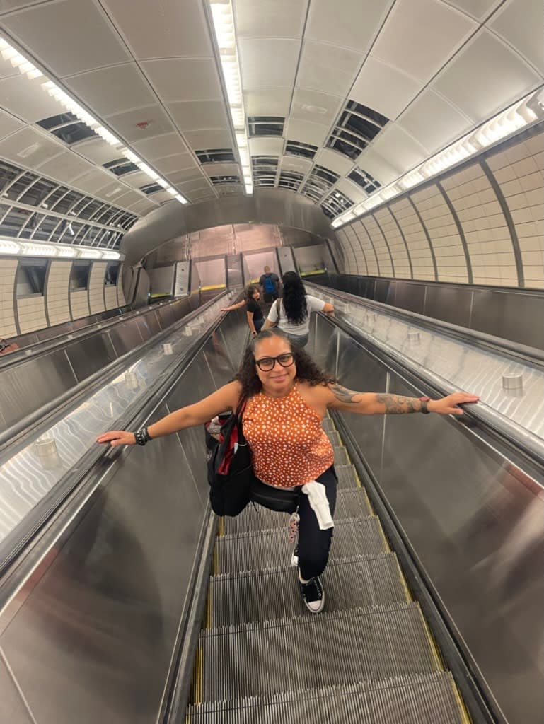 Picture of Lydia from above wearing an orange shirt and standing on an escalator