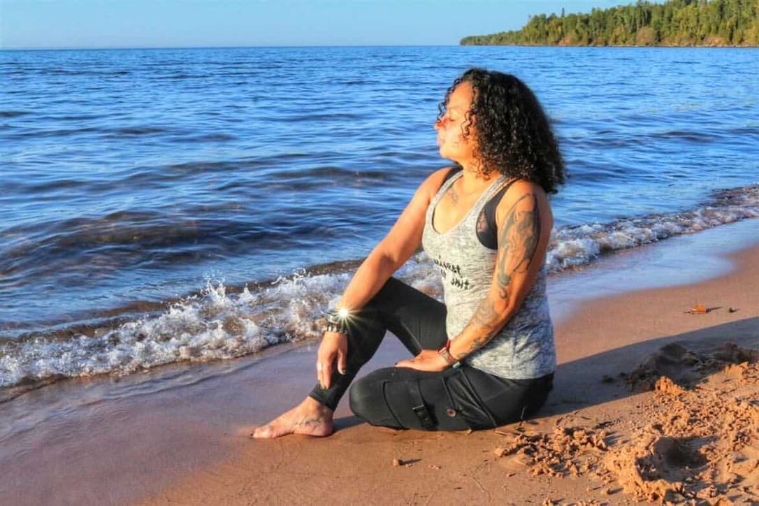Lydia sitting on the sand at the beach with her eyes closed and facing the sun