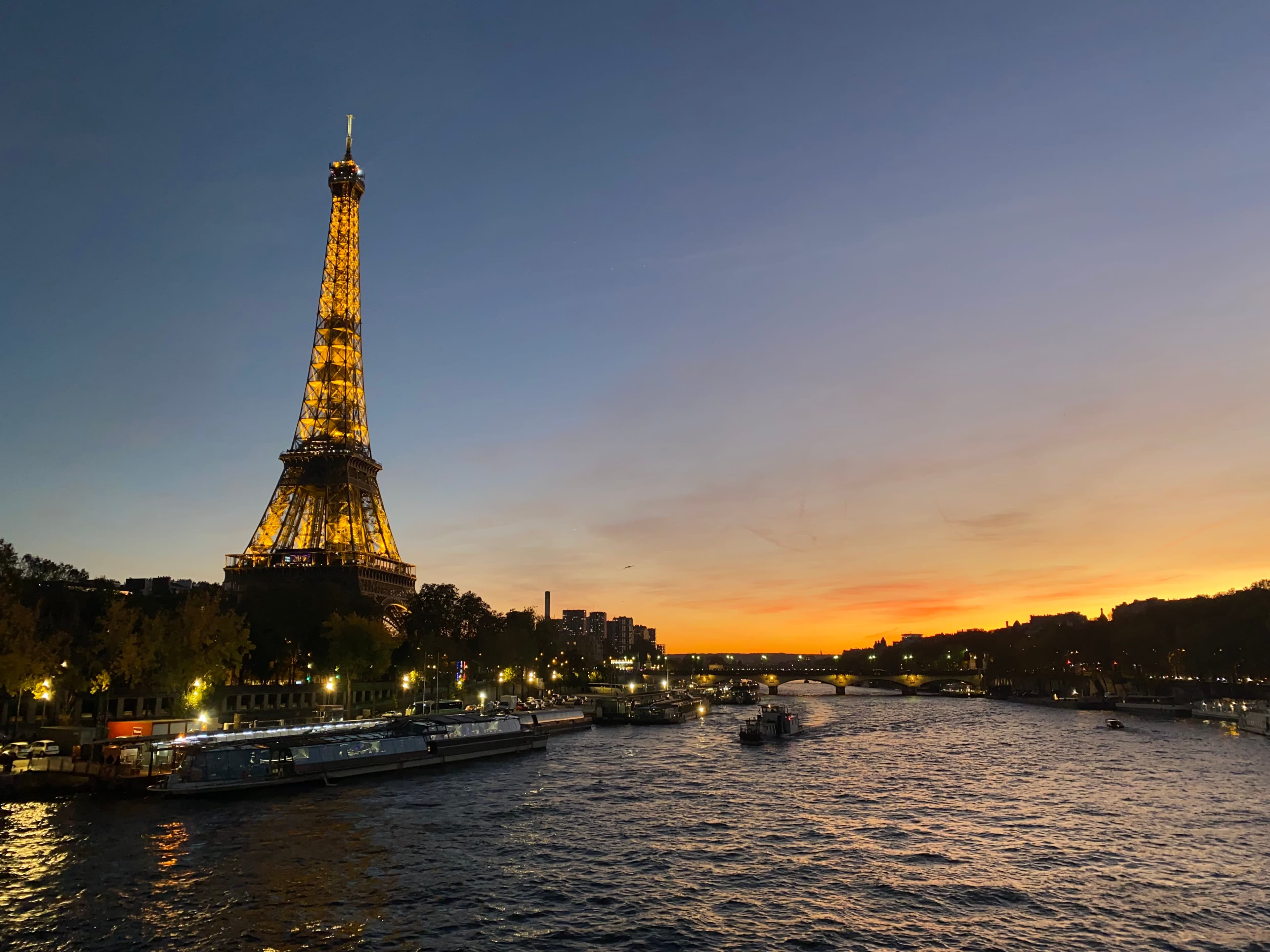 View of a lit up Eiffel Tower from the river Seine under an orange sunset